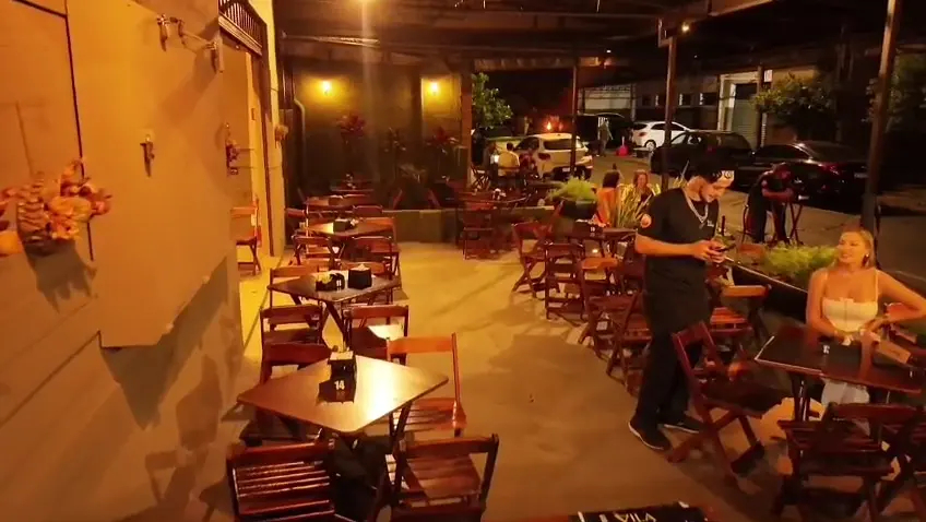 Varanda do Vila Bohêmia à noite, com mesas de madeira sob luzes quentes